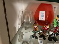 Large orange glass goblet, smaller clear goblet, three colorful clown figurines, and two small clear glass animal figurines on a shelf.
