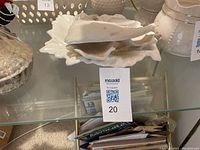 Photo showing three ceramic decorative items: a large white leaf-shaped dish, a smaller Holley leaf dish, and a fish plaque, placed on a glass shelf.
