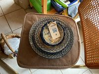 Photo showing a stack of one large serving bowl with four smaller bowls inside, all with blue and white floral designs, placed on a brown cushion on a wooden chair.