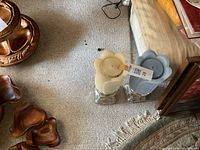 Photo showing two battery operated pedestal candles, one white and one blue, each standing on a clear glass square base, placed on a carpeted floor near furniture.