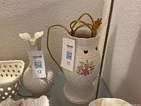 Photo showing white porcelain light with floral motif, electrical cord, and plug, alongside other porcelain items not included in lot.