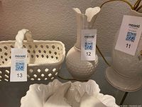 White porcelain vase with textured body and fluted rim, tagged with lot number 12; also visible other ceramic pieces including a basket and another vase.