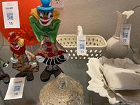 Photo showing porcelain basket centered among other decorative items including clown figurines and glassware. Basket is white with a woven texture and handle.
