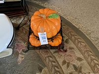 Pumpkin serving set with four small bowls and one large serving dish with lid, all ceramic, vibrant orange with green leaf accent, displayed in black wire rack.