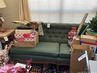 Photo of a green sofa with tufted back, wooden legs, and two seat cushions.