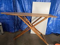 Full side view of the wooden ironing board showing the foldable X-stand and board surface.