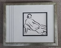 Framed black and white minimalist line art of a reclining woman on a sofa, shown flat on carpeted floor.