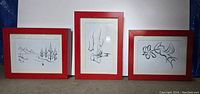 Set of 3 framed wall art prints displayed upright against a white background, with red wooden frames, showing a landscape, feet, and floral drawing.