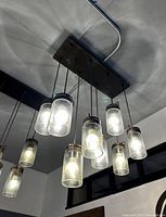 Photo from below showing one of the eight-bulb pendant light fixtures illuminated with clear glass cylinder shades and dark bronze mount.