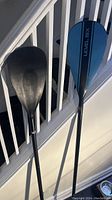 Photo showing two adjustable paddles leaning against a banister, one paddle with a blue blade marked 'LEVEL SIX' and the other paddle completely black.