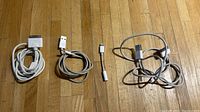 Three Apple charging cables and one Lightning to headphone jack adapter laid out on wooden floor.