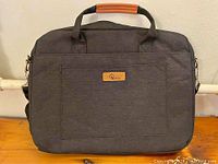 Front view of black E-Tree laptop bag showing the brown leather handle accent and front zipper pocket with E-Tree logo patch.