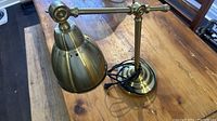 Full view of brass-coloured IKEA Barometer work lamp on wooden surface, with adjustable arm and head visible.