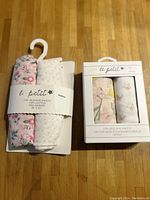 Two sets of baby muslin blankets side by side. Left: 2-pack of 100% cotton pre-washed blankets with pink floral and gray dotted patterns. Right: 2-pack bamboo muslin blankets with floral and butterfly print and yellow animal pattern in original packaging.