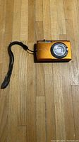 Front view of the Nikon Coolpix S3000 orange digital camera showing lens and wrist strap.
