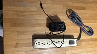 AC/DC adaptor and Belkin power bar side by side on wooden floor, showing the items in use-ready position.
