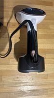 Lateral view of the Rowenta handheld fabric steamer showing white body, black foldable handle and base, tilted on wooden surface.