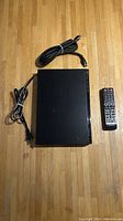 Black Samsung BD-J4500R Blu-ray/DVD player with power cable, HDMI cable and remote control laid out on wood floor.