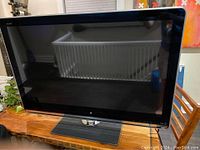Front black glass screen of the 40 inch Sharp Aquos TV sitting on a wood table with a thick rectangular base stand.