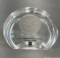 Front view of thick clear glass paperweight with embedded 1998 American Silver Eagle 1 oz silver coin and etched text 'U.S. Dollar Funds Launch October, 1998' with logo on the base
