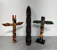 Group photo of two colorful miniature totems and one carved dark wood totem pole.