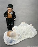 Photo showing Bill Sikes figurine and baby in cradle figurine side by side on a grey surface.