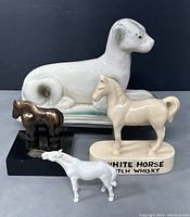 All four animal figurines grouped. Three horse figurines and one dog figurine shown from the front on grey surface with dark background.