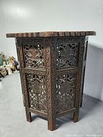 Side view of hand carved octagonal folding table showing detailed floral panels and legs.