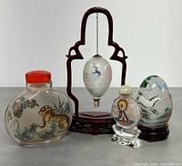 Overall group shot of four Chinese reverse painted snuff bottles and snuff egg with wooden display stand on white background.