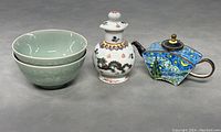 Set of green ceramic bowls, dragon snuff bottle, and multi-sided cloisonne enamel teapot on grey background