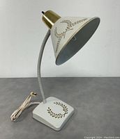 Mid-Century Modern aluminum gooseneck desk lamp painted white with gold leaf motif on shade and base, brass collar, flexible neck, power cord with inline switch.