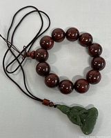 Photo showing the dark brown polished round wood beads strung on a cord with the green carved jade Buddha pendant attached.