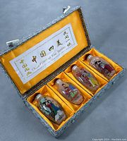 Original box open showing four glass snuff bottles in yellow satin compartments with label on the lid