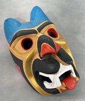 Front angle showing colorful painted carved native mask with pronounced facial details and tongue sticking out.