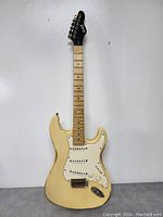 Full view of cream-colored Slick electric guitar solid body with maple fingerboard and black headstock. Shows wear and signs of aging on body and neck.