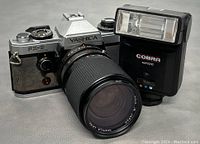 YASHICA FX-D film camera front side with attached zoom lens and Cobra Auto 210 flash unit placed upright beside it.