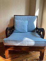 Front view of dark wood armchair with blue cushions and lumbar pillow, showing detailed wood carving on armrests and cushion texture.