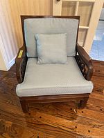 Front view of the chair showing blue seat and back cushions along with a matching decorative pillow on wooden frame.