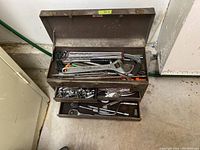 Wide view of open metal toolbox showing assortment of tools inside with two trays.