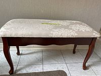 Side view of cherry wood bench with floral off-white upholstered seat, showing cabriole legs.