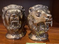 Pair of detailed brass lion head bookends shown from the front with roaring expressions, polish and patina visible.