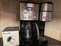 Front view of Cuisinart coffee maker with glass carafe, digital controls, and Breville frothing jug box.