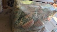 Full view side angle of the couch wrapped in protective plastic wrap showing floral upholstery pattern and shape.