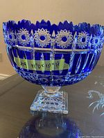 Front side view of a blue cut crystal bowl showing starburst patterns, scalloped rim, and square pedestal base with measurement taped on the side.