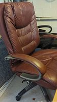 Side view of brown leather swivel desk chair showing padded armrest, seat, and backrest, and adjustment lever.