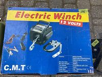 Blue product box with Electric Winch 12 Volts branding, C.M.T brand, and product specs including 6000lb rolling capacity, 5000lb pulling capacity, 18ft max boat size, 30ft cable length, and 12 volts power supply.