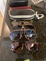 Four pairs of eyewear and three cases arranged on a granite counter showing different styles and colors of glasses.