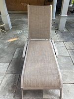 Front view of the outdoor lounge chair showing beige fabric mesh seating and metal frame.