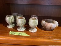 Front view of six marble liqueur glasses and one candy bowl showing natural color veining and shape.