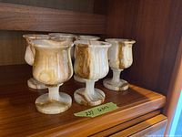 Six marble wine goblets arranged on a wooden shelf, showing various angles and natural stone patterns.